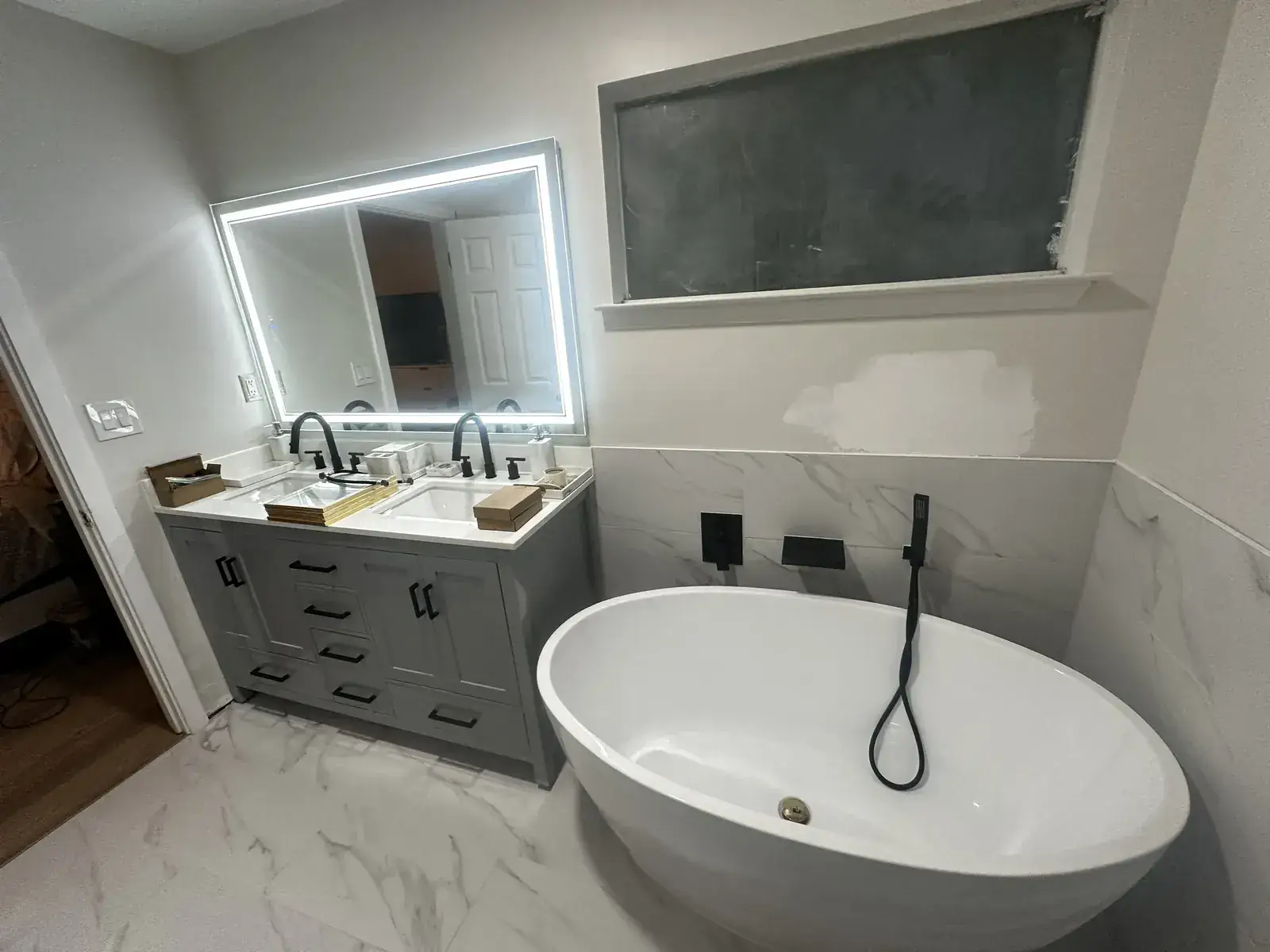 Freestanding tub with floor-mounted matte-black filler, LED mirror and gray vanity