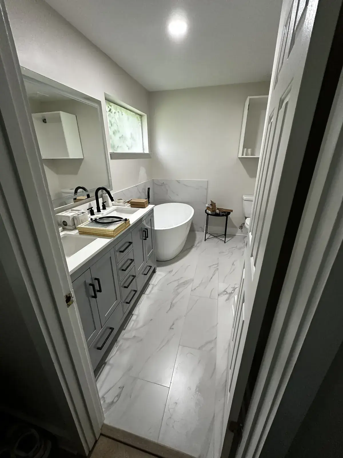 Remodeled master bath with freestanding soaking tub, marble-look porcelain tile and gray double vanity