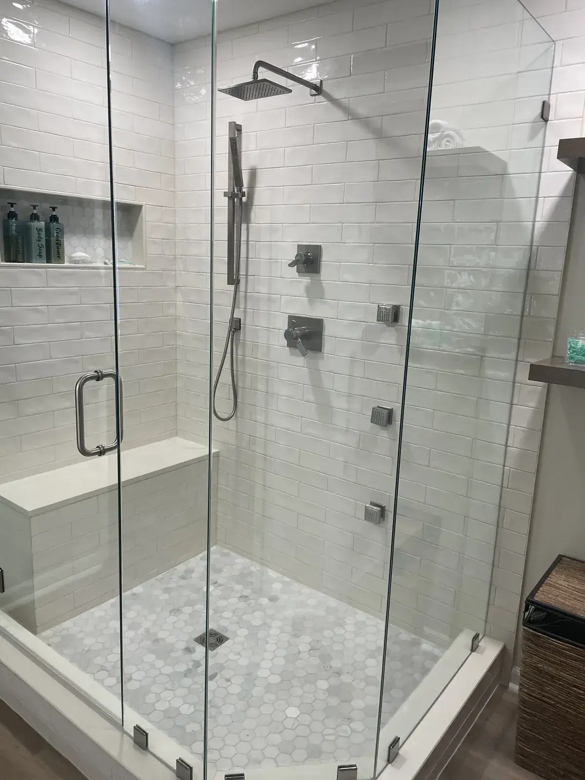 Frameless glass walk-in shower with subway tile, built-in bench, niche, rain head and marble hex floor