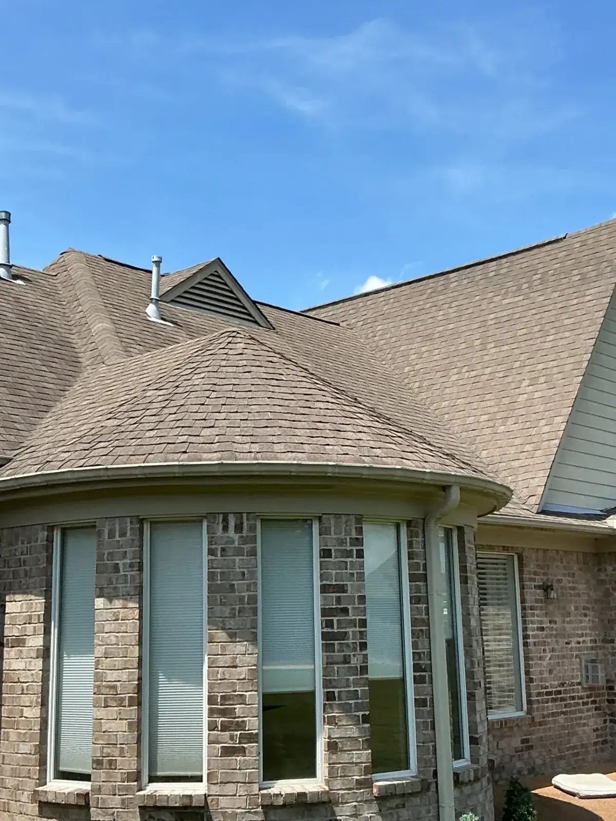 Finished architectural shingle roof over a rounded brick bay window with gable vent, blue sky