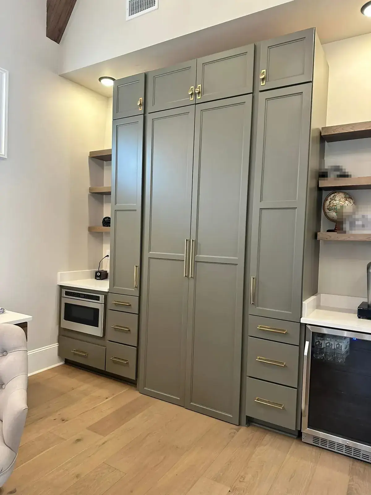 Greige floor-to-ceiling built-in pantry wall with brass pulls, beverage fridge and floating oak shelves