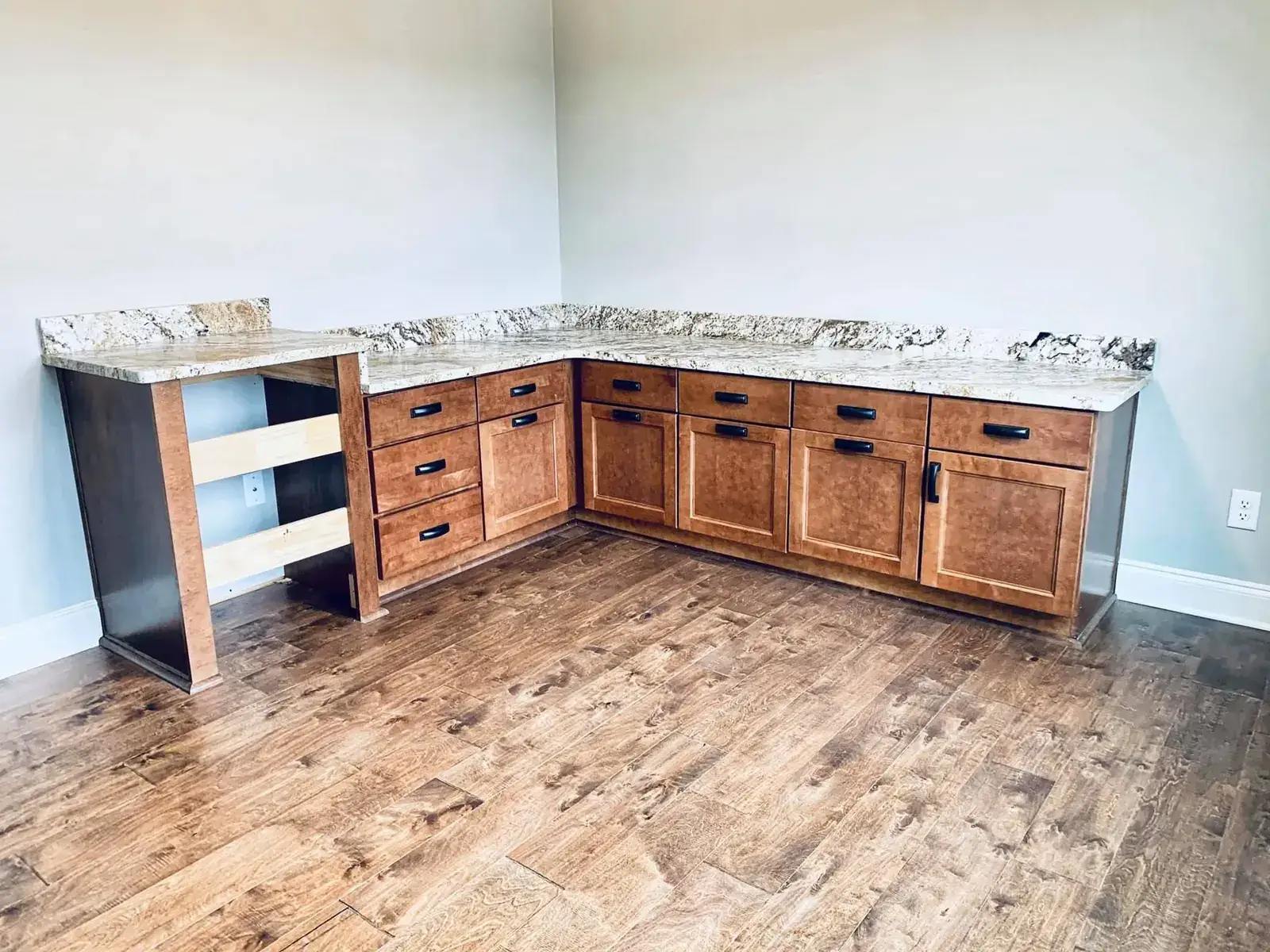 Maple base cabinets with granite top wrapping into a desk corner over hand-scraped wood floors