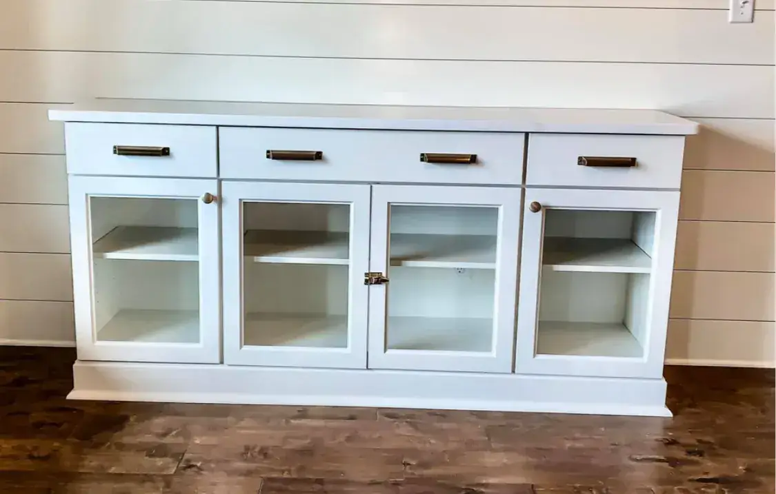 Custom white sideboard buffet with glass doors and brass cup pulls against shiplap