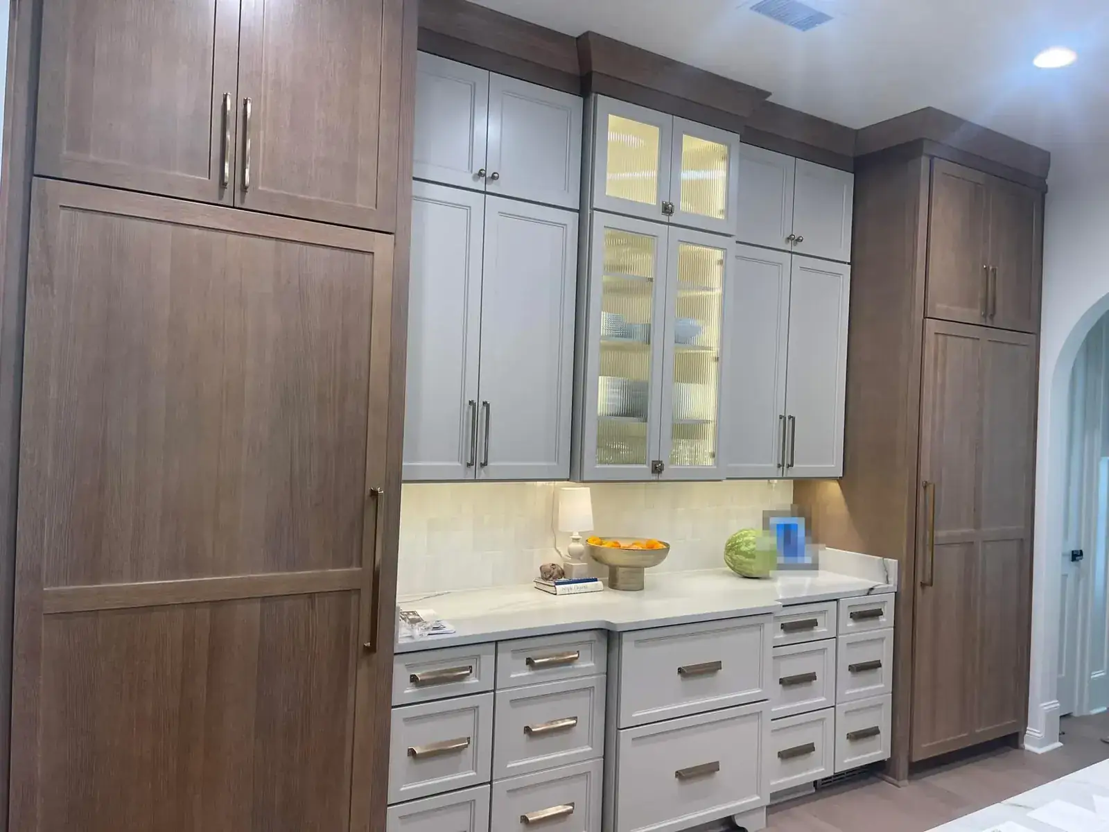 Built-in coffee bar with rift-oak panel cabinets, gray uppers with reeded glass and brass pulls