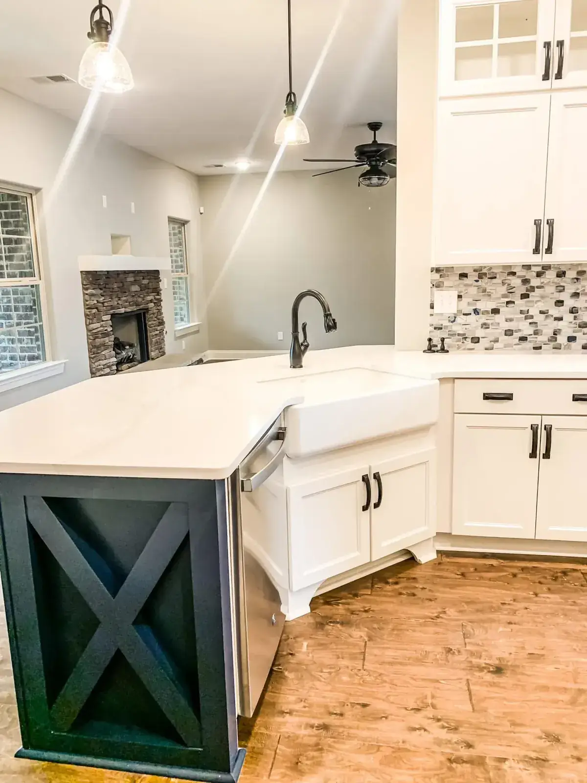 White kitchen with farmhouse sink peninsula, navy X-panel end, mosaic backsplash and stone fireplace beyond