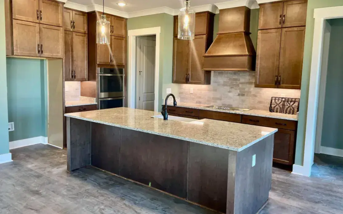 Warm wood-cabinet kitchen with granite island, copper-toned range hood, stone backsplash and glass pendants