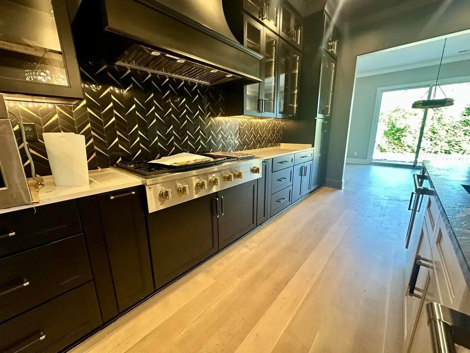 Pro range with brass knobs under a black hood, black-and-gold chevron backsplash and lit glass uppers