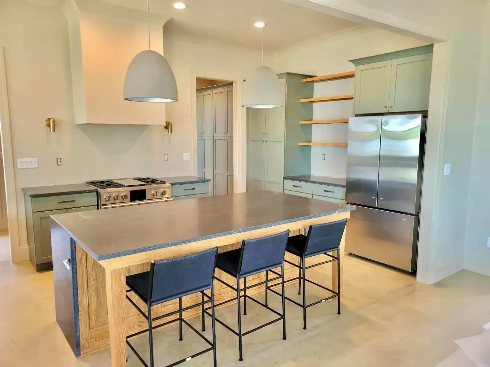 Sage-green shaker kitchen with oak-base island and soapstone-look top, open oak shelves and dome pendants