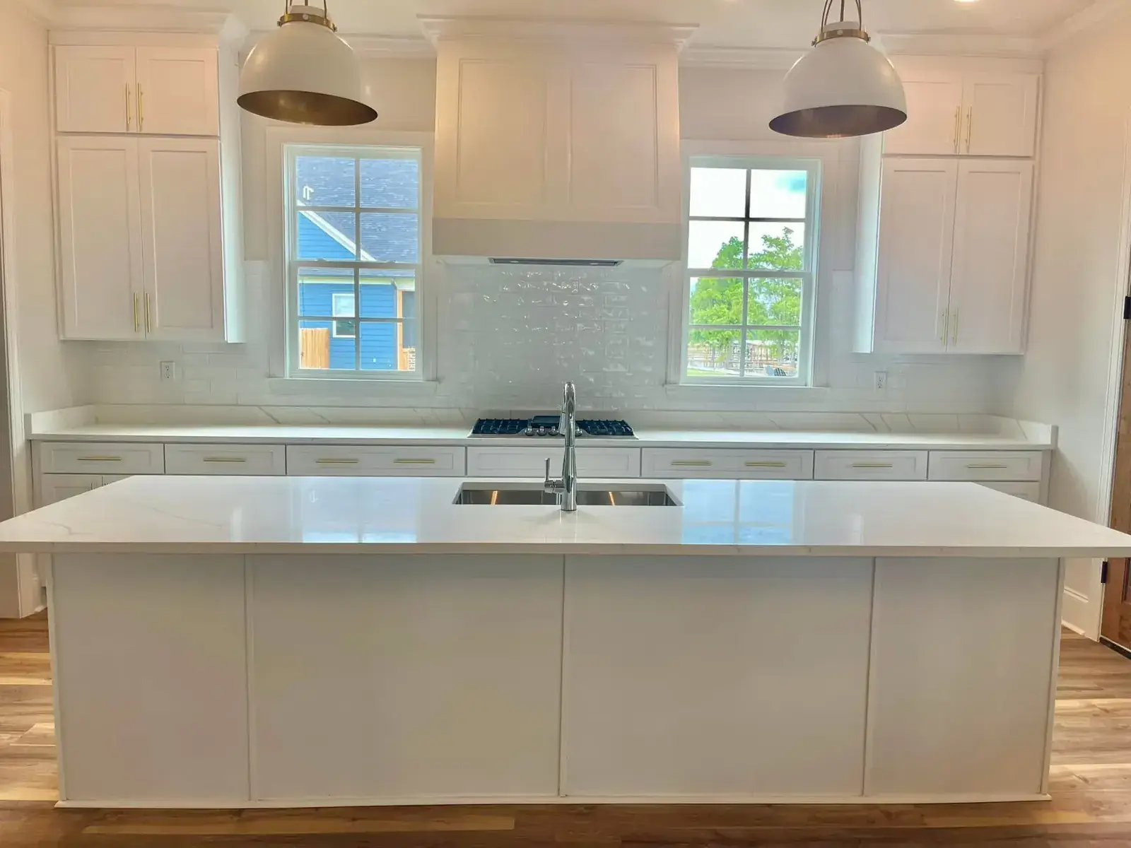 All-white kitchen with long quartz waterfall-style island, brass-lined dome pendants, subway tile and twin windows