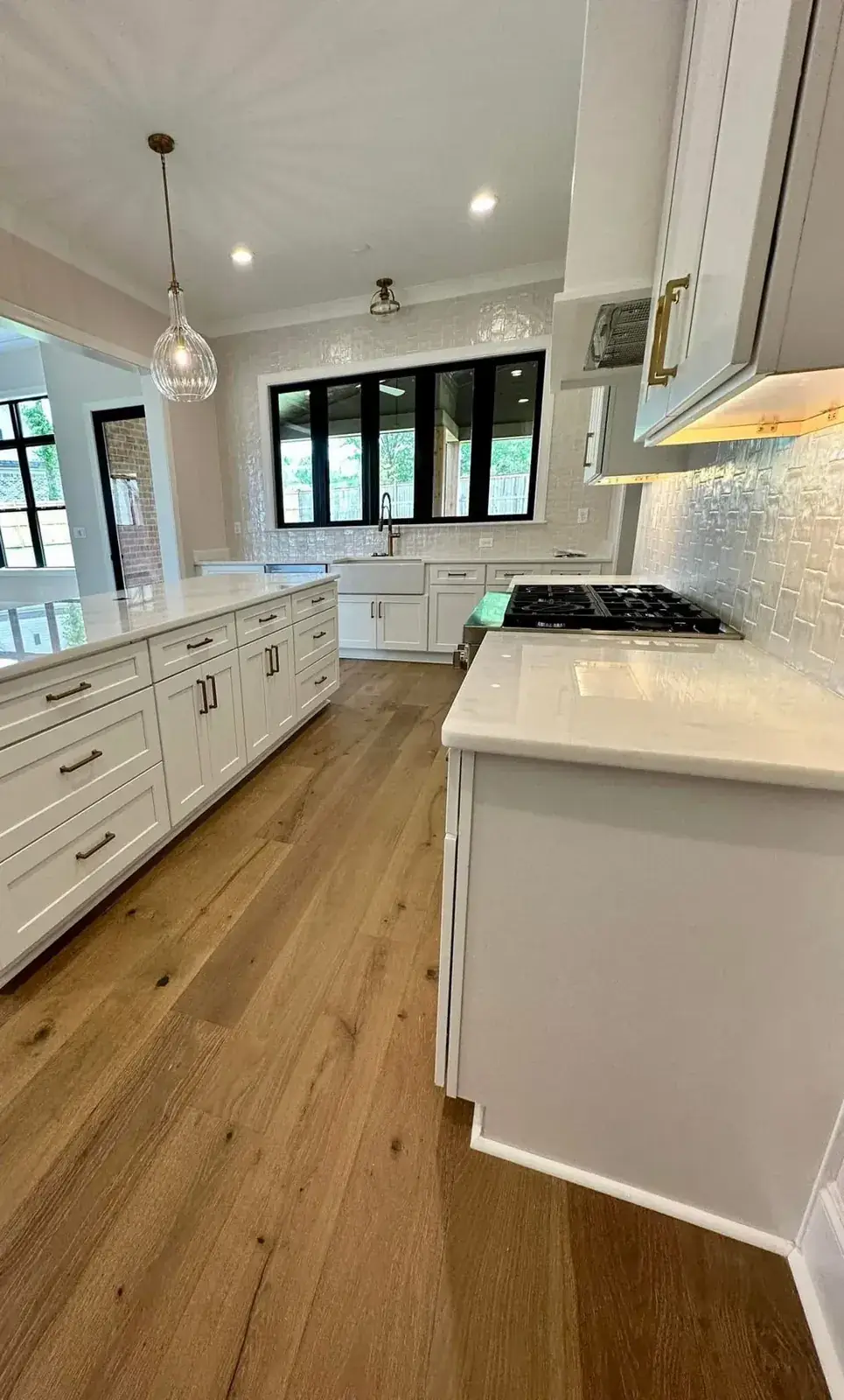 White shaker kitchen with long island, gas cooktop, handmade-tile backsplash and wide-plank white-oak flooring