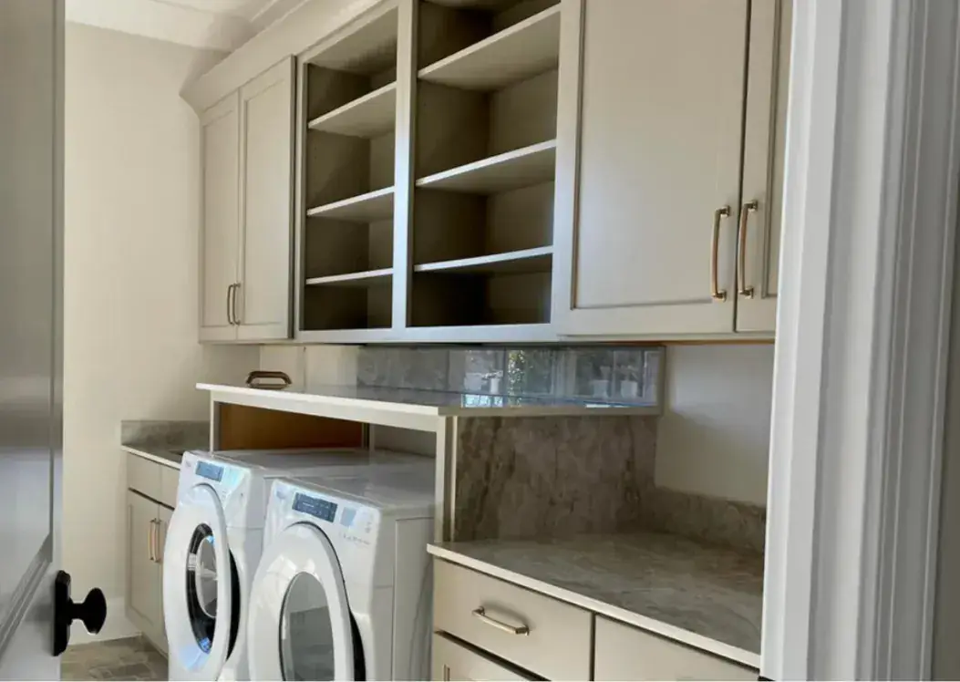 Laundry room with greige cabinets, open cubbies, quartzite folding counter and front-load pair