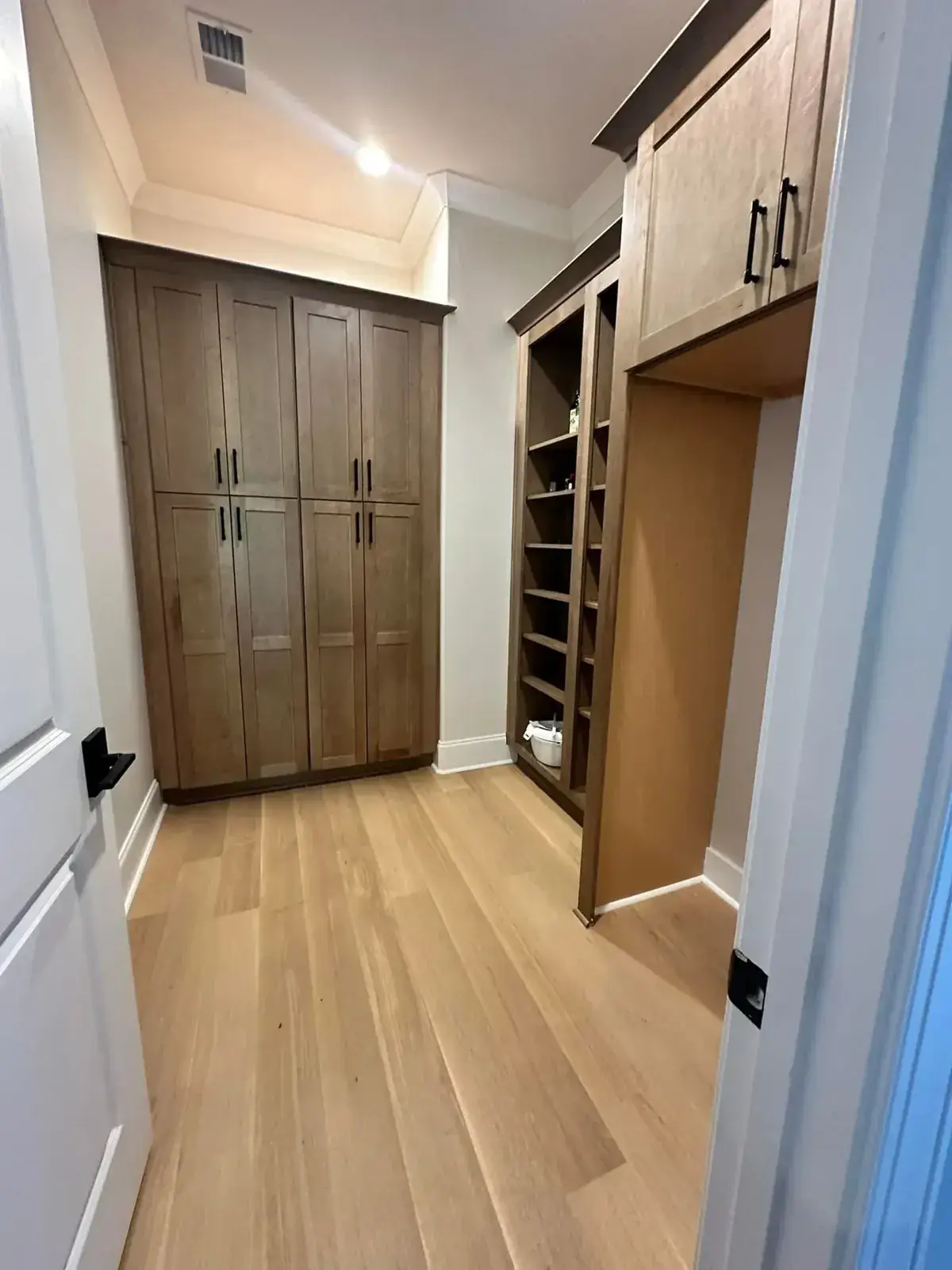 Walk-in pantry with stained oak tall cabinets, open shelving and white-oak floors