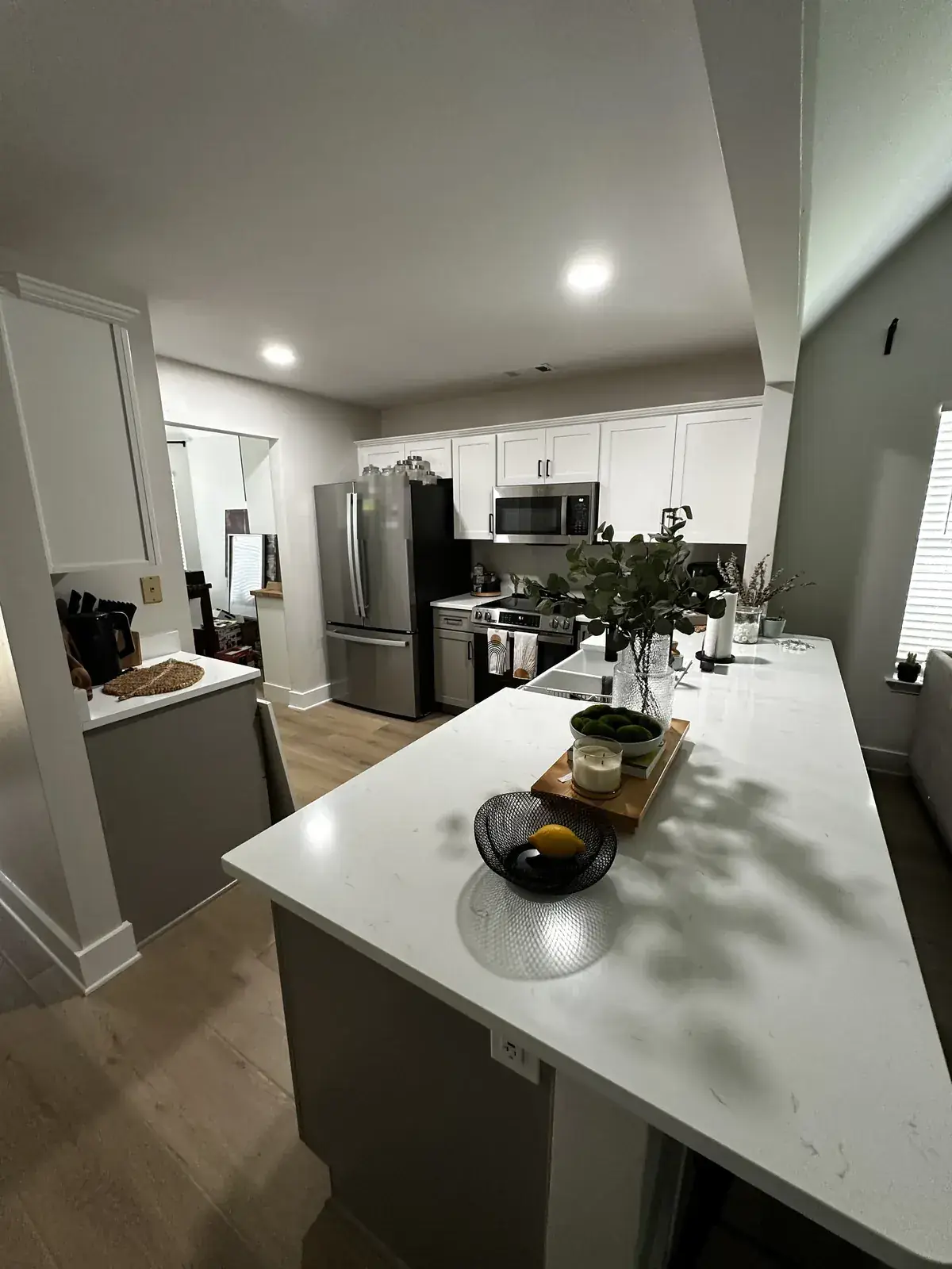 Finished kitchen with long quartz island, white upper cabinets and stainless appliances