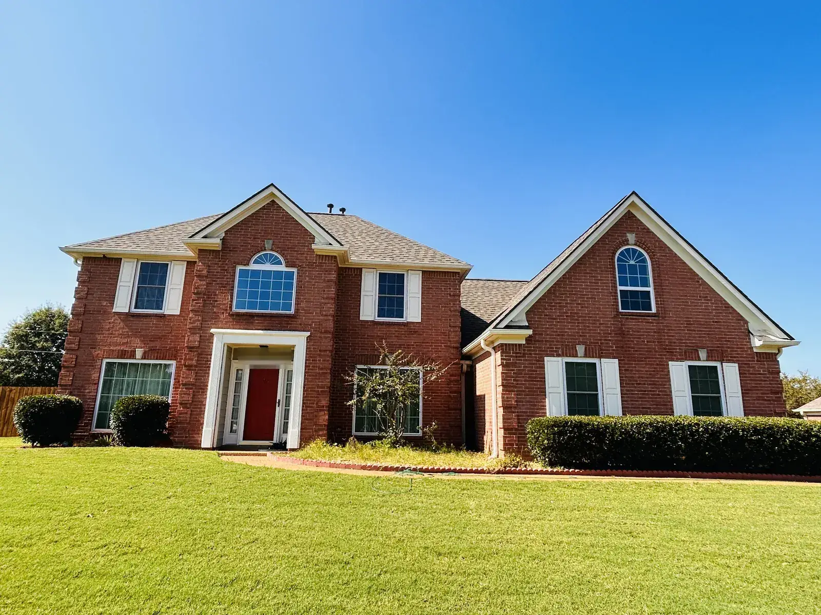 Same brick home from a straight-on angle showing the finished architectural shingle roof lines, gables and ridge