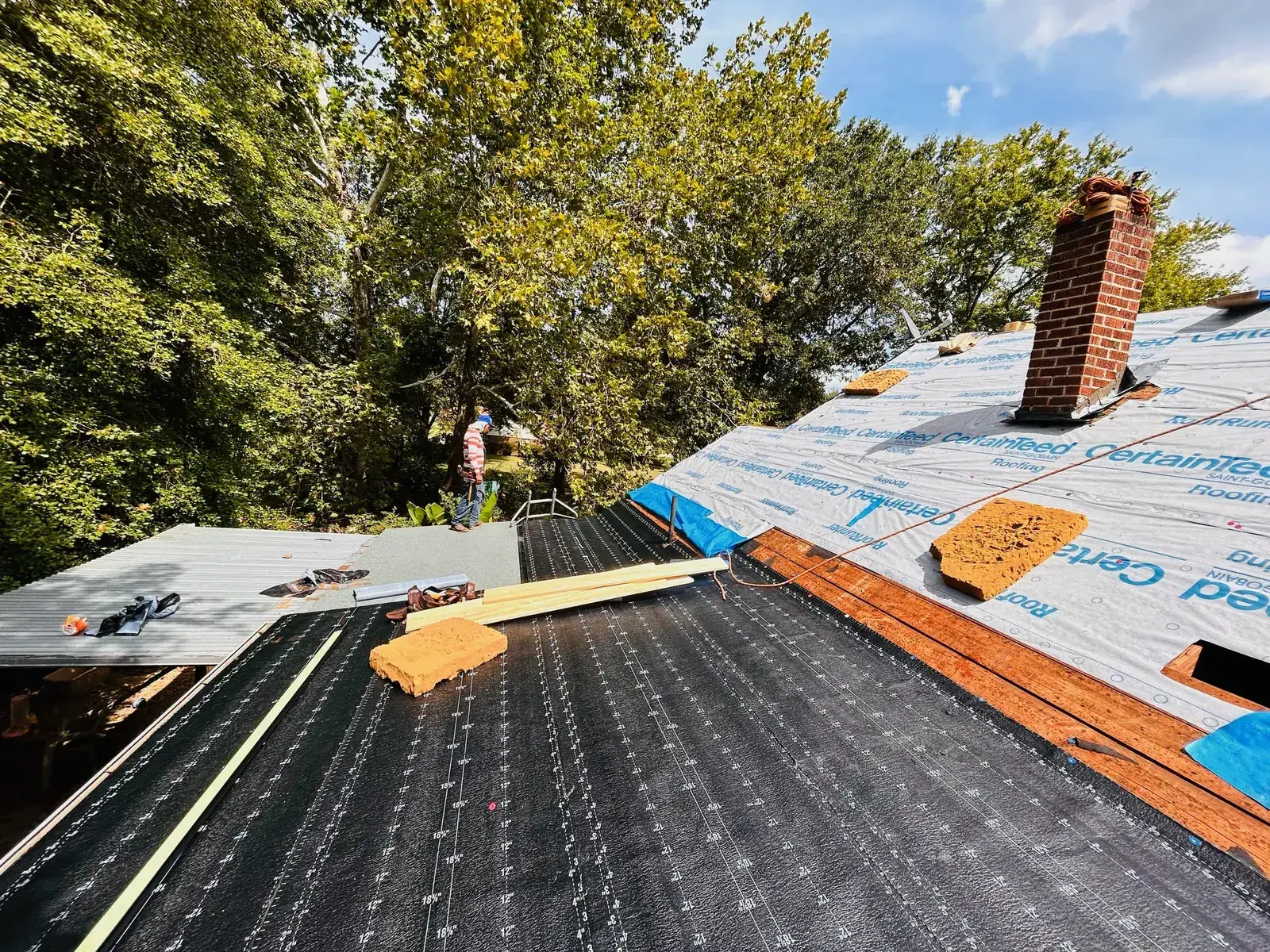 Crew installing a new roof on a large brick home, pool protected with tarps and ladders staged, shows jobsite care